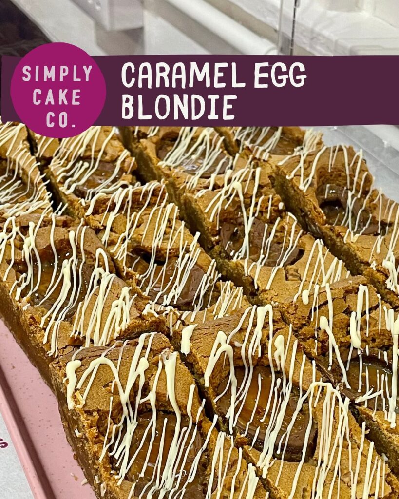Tray of Simply Cake Co’s Caramel Egg Blondie bars topped with gooey caramel-filled chocolate eggs, golden blondie base, and rich swirls of white and milk chocolate.