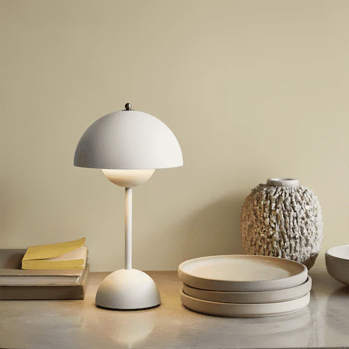 A Scandi Table Lamp on a table with books, plates and a vase of flowers.