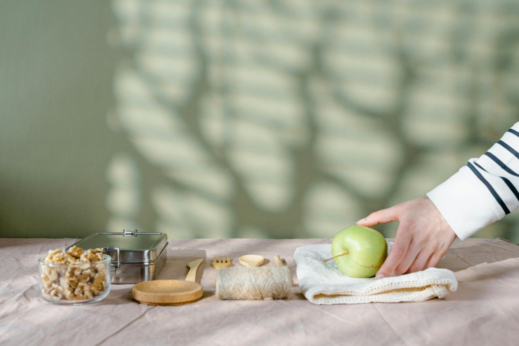 A hand holds a green apple on a table set with snacks, ideal for healthy eating themes.