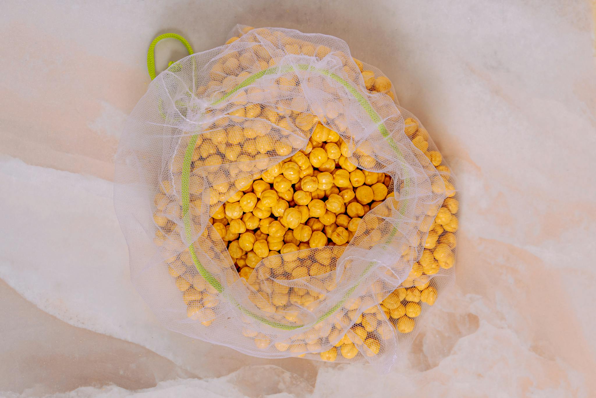 A top view of yellow chickpeas in an eco-friendly mesh bag on a neutral background.