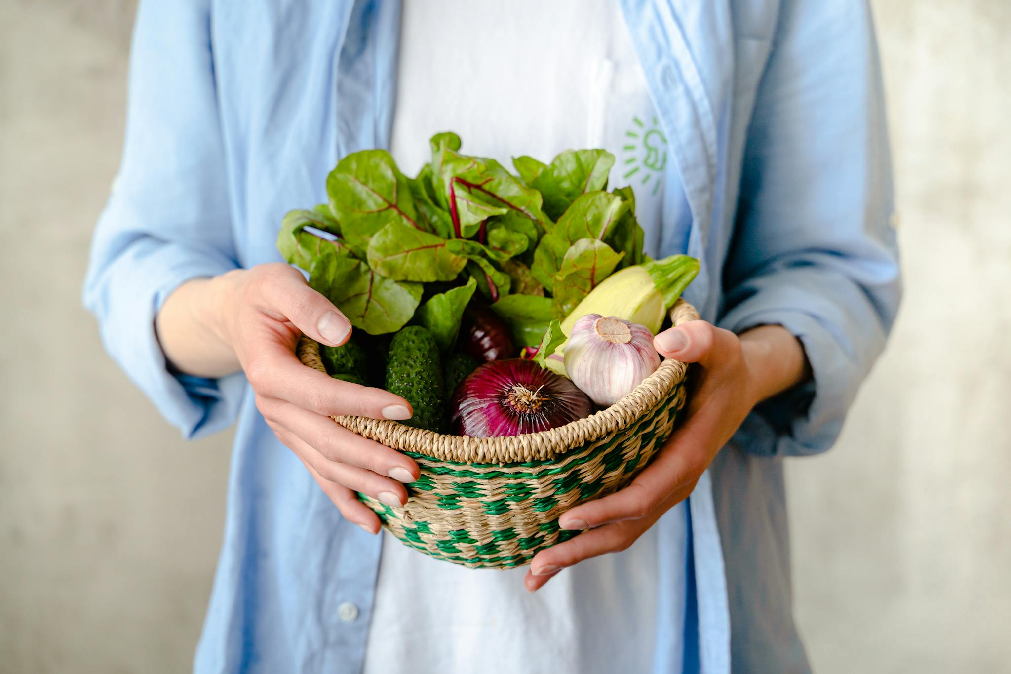 Person holding a basket of ethically sourced healthy food products including leafy greens and garlic