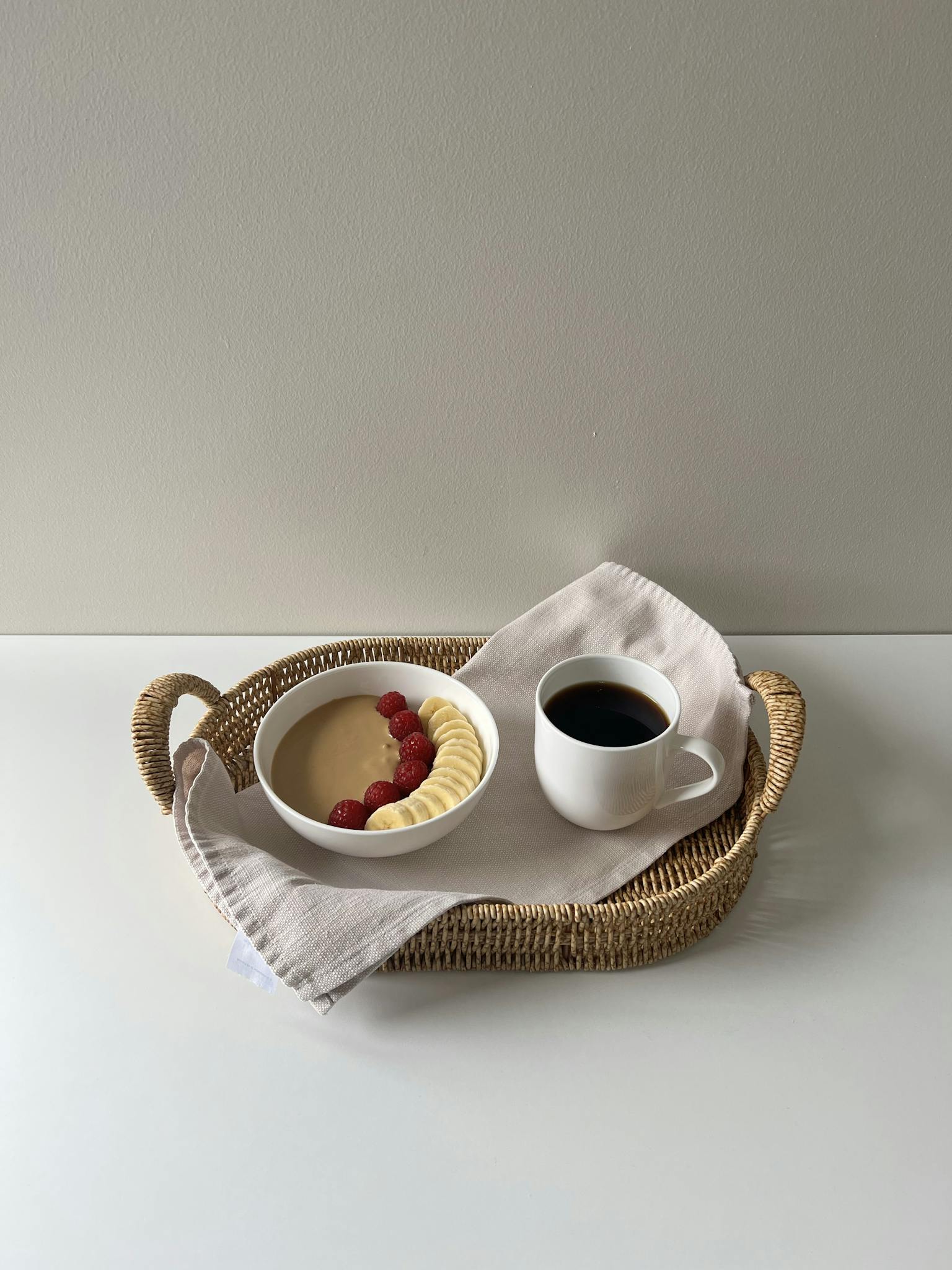 Minimalist breakfast tray with coffee and fruit smoothie bowl on white table.