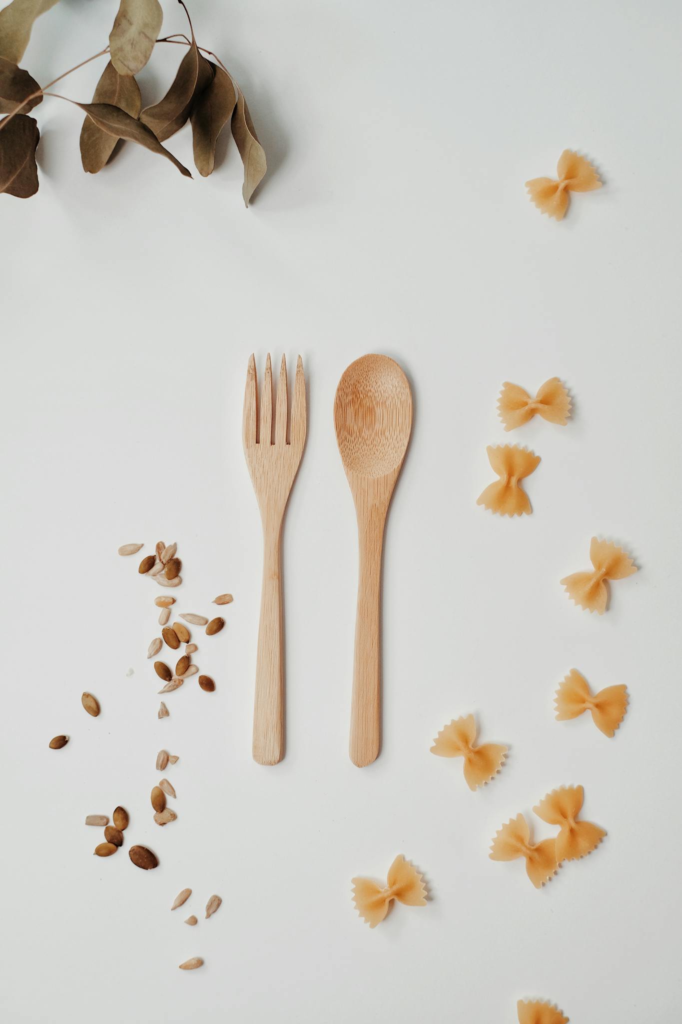 Wooden fork and spoon with farfalle pasta on white background, perfect for kitchen decor.