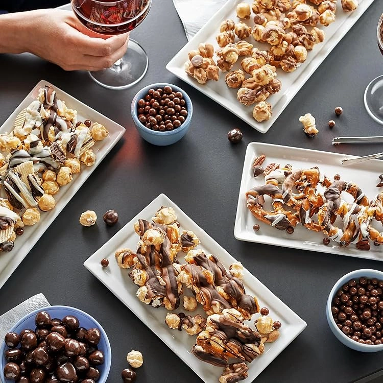 Elegant display of Funky Chunky gourmet popcorn and pretzel clusters drizzled with chocolate, served on white rectangular plates with bowls of chocolate-covered treats, paired with glasses of red wine for a luxurious corporate gifting presentation.